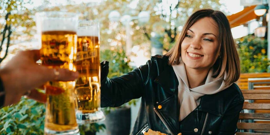 Happy woman toasting with beer in a restaurant, relaxed date with escort service, conversation and laughter - stylish female companionship, outdoor dining, social occasion, friendly meeting, bar scene, social interaction, elegant companionship, beautiful woman with brown hair, stylish outfit, friendly environment, convivial gathering.